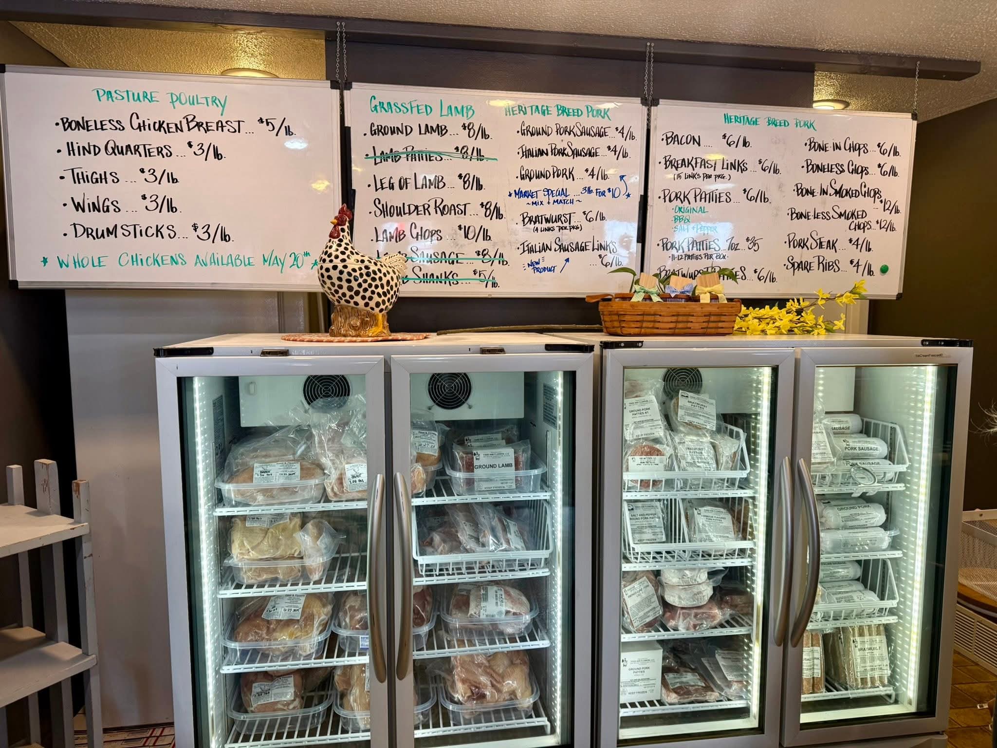 Four glass-door refrigerated display cases filled with packaged food products, set in front of three white menu boards with handwritten prices and items.